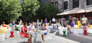People socializing and dining at a stylish Beacon Hill venue, surrounded by greenery and flowers on a sunny Massachusetts day.