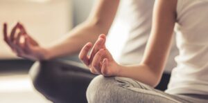 Two people sit cross-legged on the floor, meditating with hands resting on knees and fingers in a mudra position.
