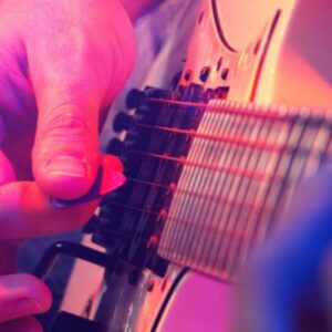 Close-up of a person playing an electric guitar in a luxury Massachusetts suite, fingers skillfully strumming under vibrant, colorful lighting.