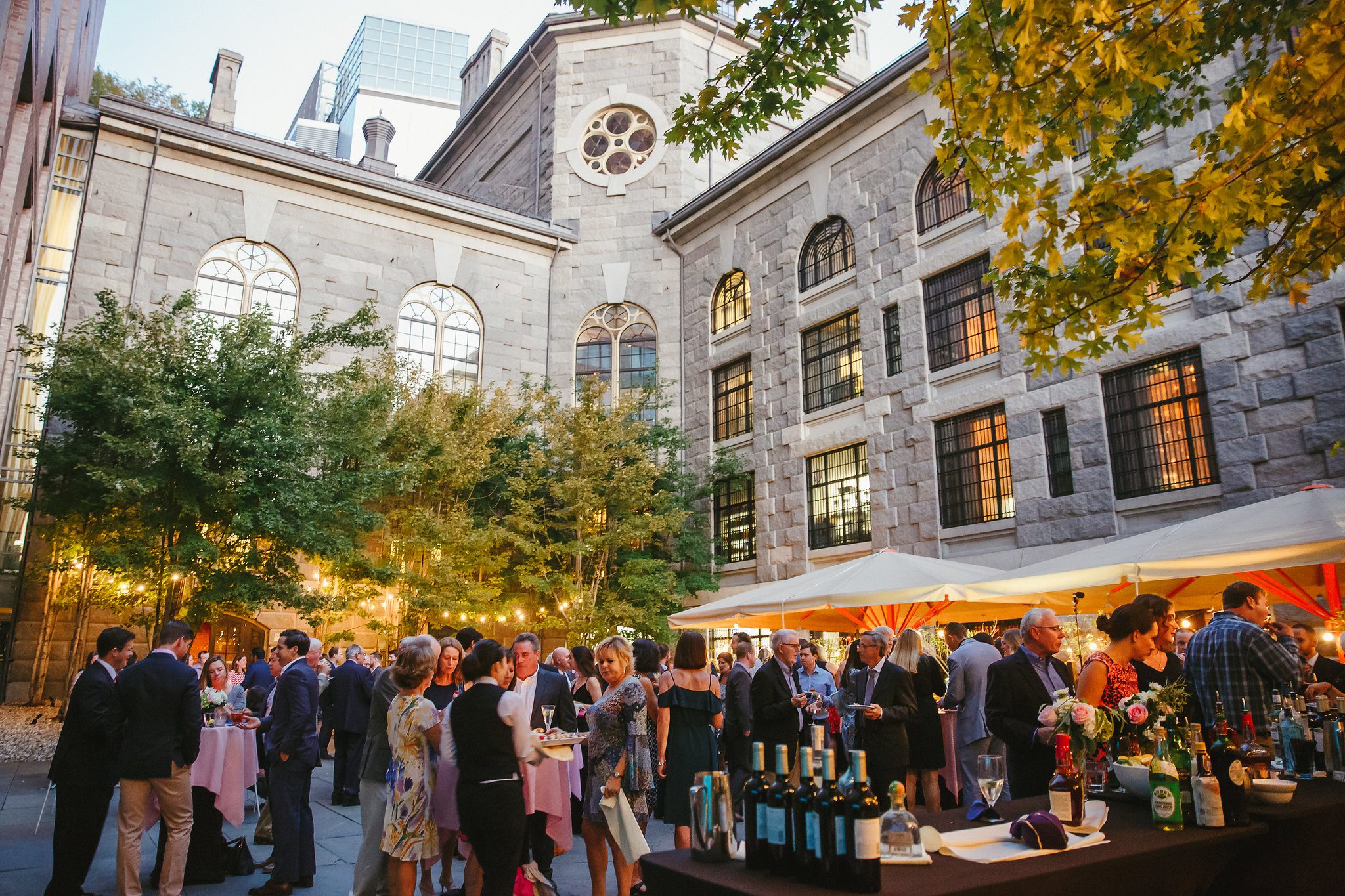 Elegant private event in a courtyard near Boston Common with people mingling, string lights, cocktail tables, and a historic stone building backdrop.