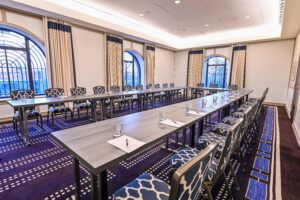 U-shaped conference table setup in a modern Beacon Hill meeting space with patterned chairs, notepads, and large arched windows letting in natural light.