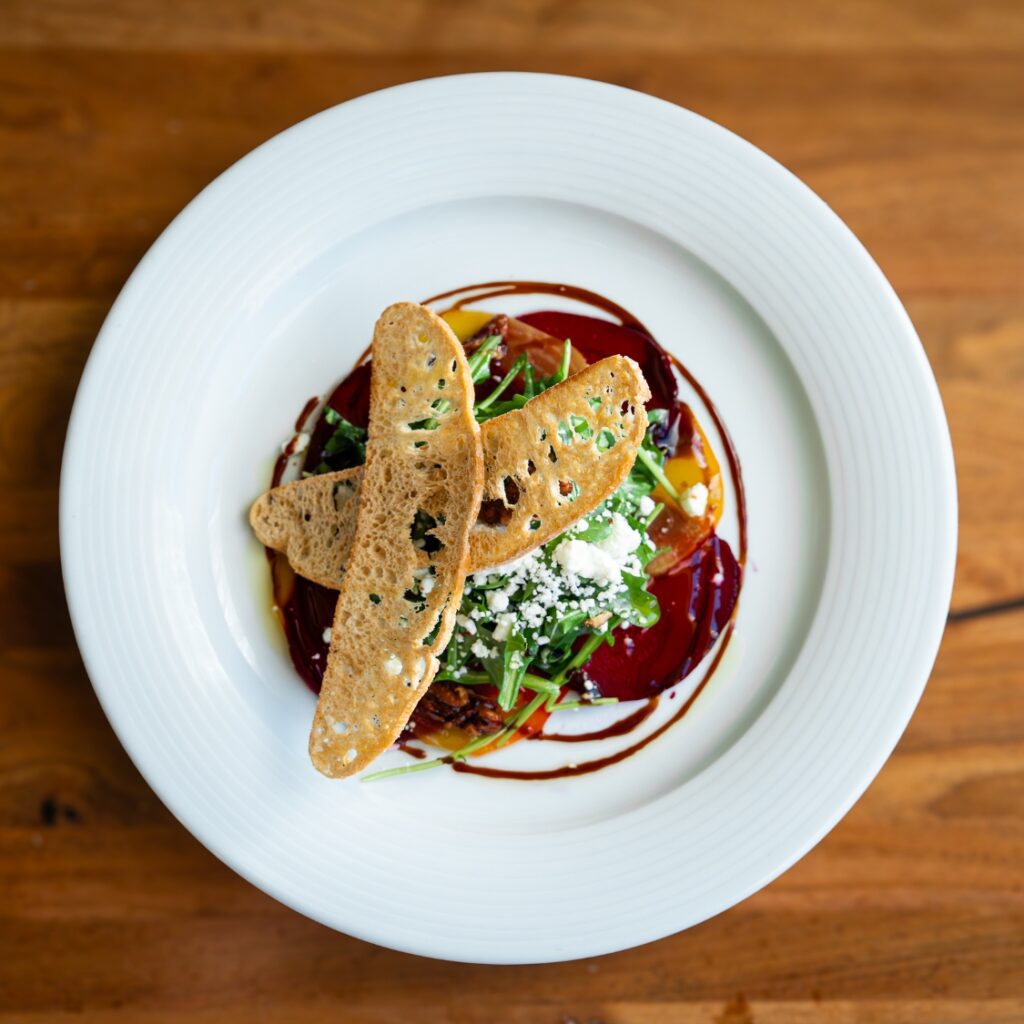 A plated salad with greens, crumbled cheese, and toasted bread, artfully served on a white plate over a wooden table in Beacon Hill, Boston.