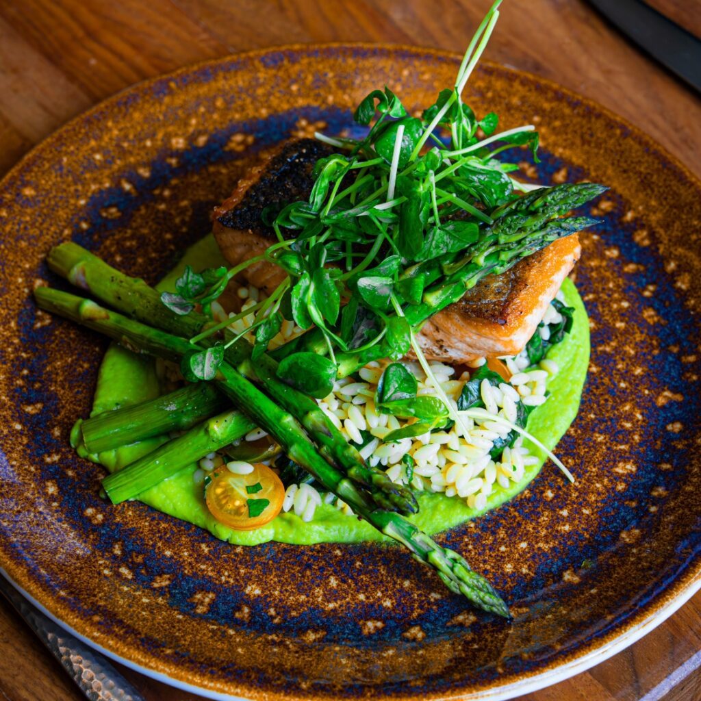 Seared salmon on orzo with microgreens and asparagus, served on a vibrant green sauce at our Beacon Hill restaurant.