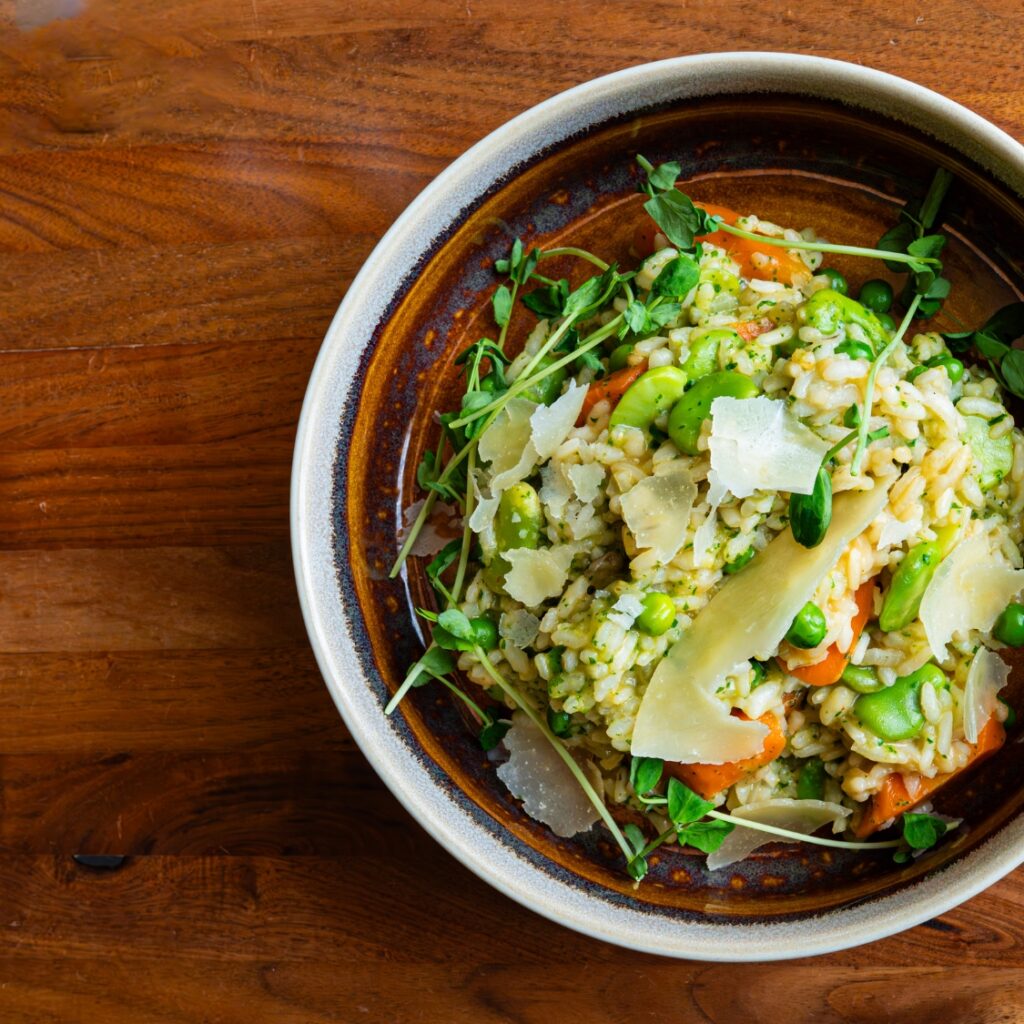 A bowl of vegetable risotto topped with shaved parmesan, peas, and greens served at a cozy restaurant near Boston Common in Massachusetts.