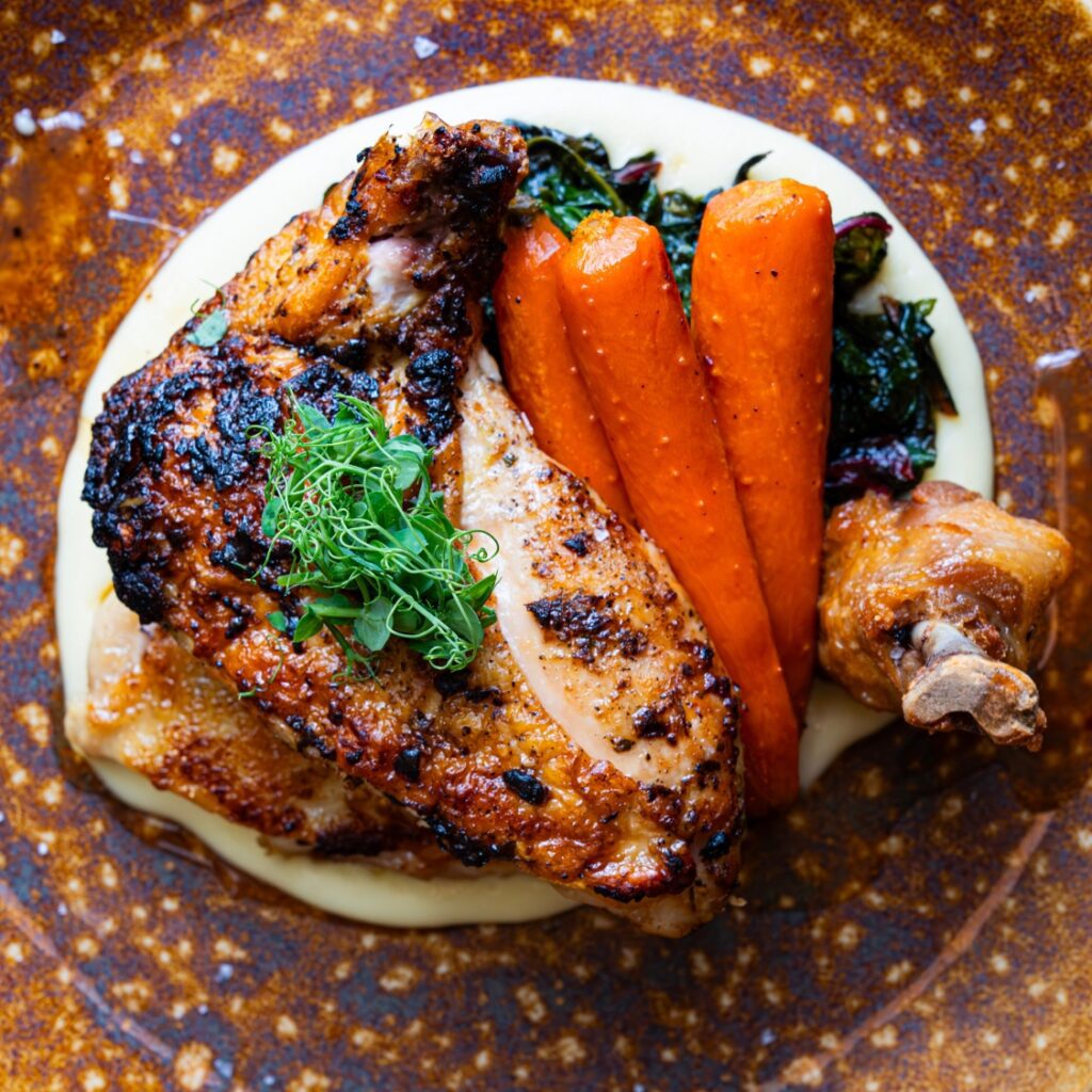 Grilled chicken with crispy skin, sautéed greens, and mashed potatoes—classic American comfort inspired by Massachusetts and Boston Common.