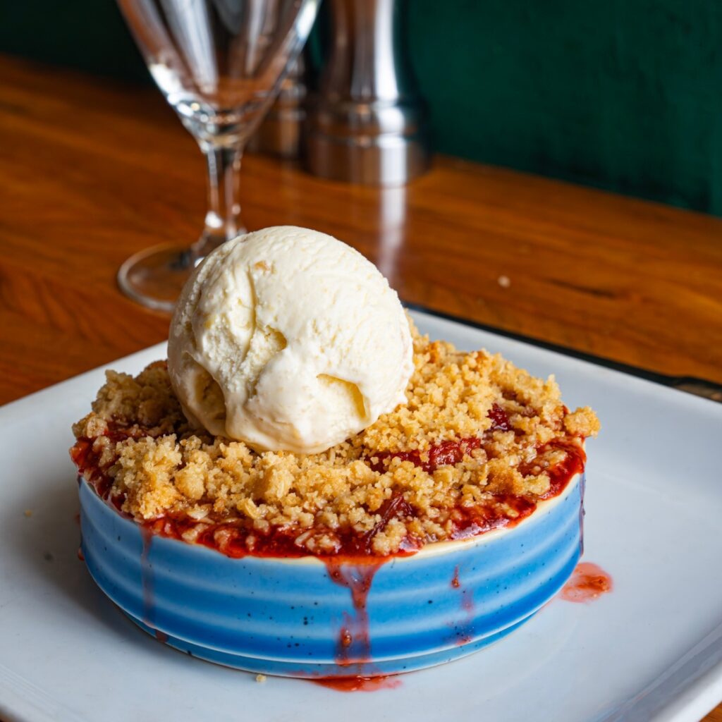 A fruit crumble topped with vanilla ice cream on a white plate, served at a restaurant near Boston Common in Massachusetts.