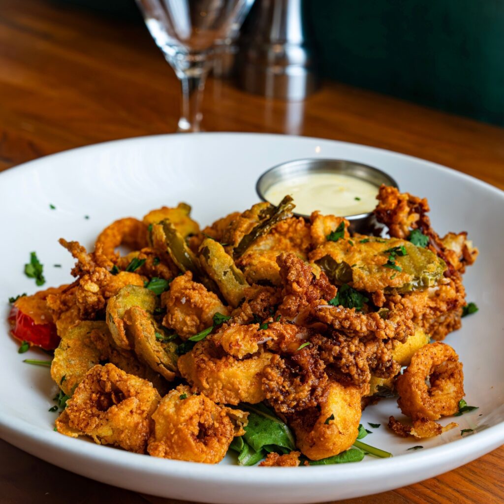 A white plate of fried calamari with peppers and herbs, served with sauce on a wooden table at our Beacon Hill restaurant near Boston Common.