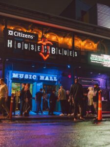People line up outside the vibrant, neon-lit House of Blues Music Hall at night, near a historic hotel in the heart of Boston.