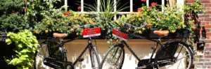Two black bicycles with brown seats are parked outside Liberty Hotel, a luxury lodging destination in Massachusetts, adorned with flowers and greenery.