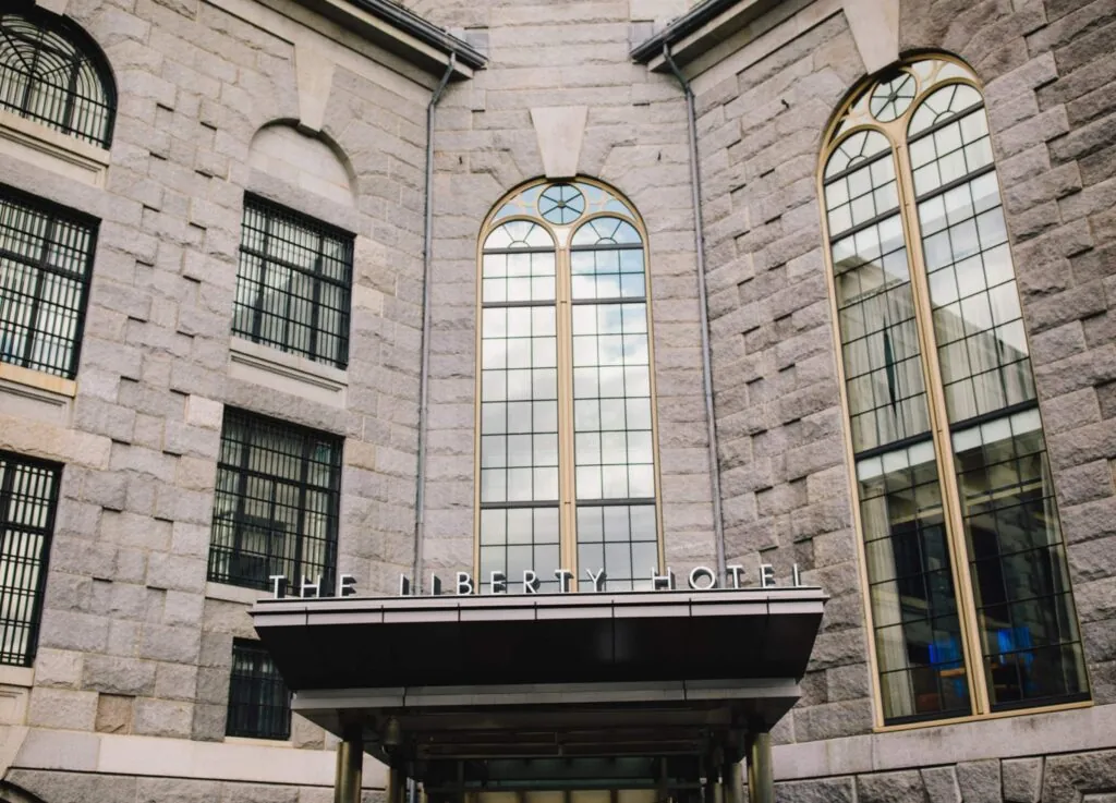 Luxury stone building facade with large arched windows and a sign reading The Liberty Hotel above the main entrance.