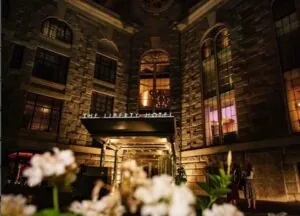The Liberty Hotel’s stone exterior and tall windows are lit warmly at night, with flowers in the foreground in luxury Beacon Hill style.