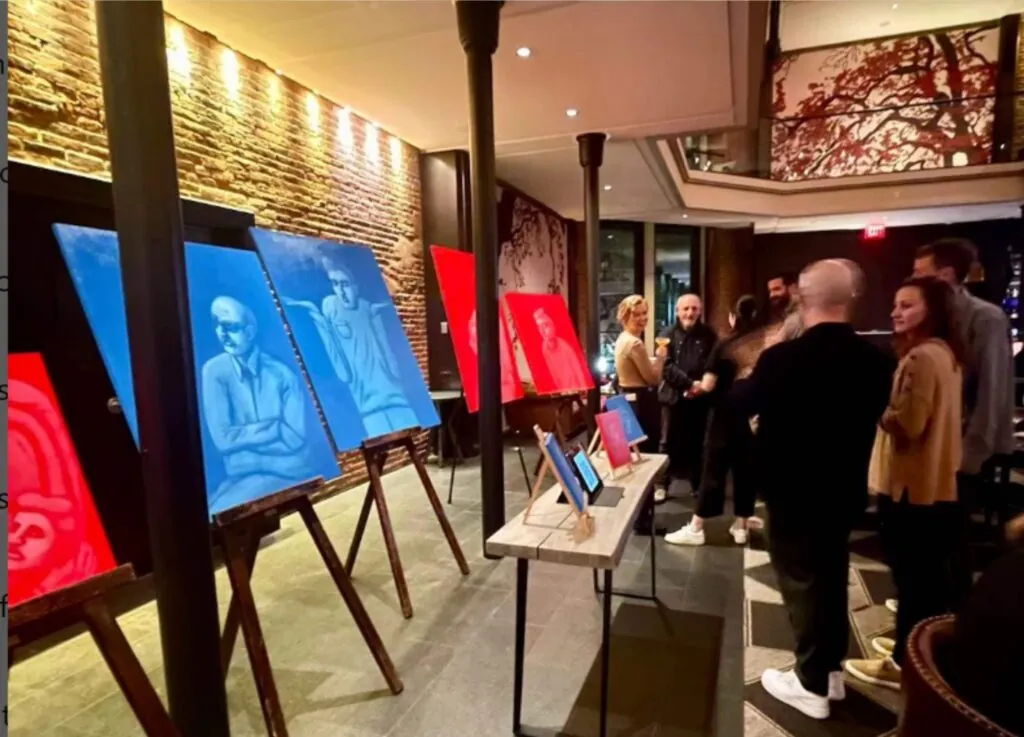 Guests at a luxury Beacon Hill hotel admire blue and red portrait paintings on easels, gathering to chat near the stunning indoor gallery artworks.