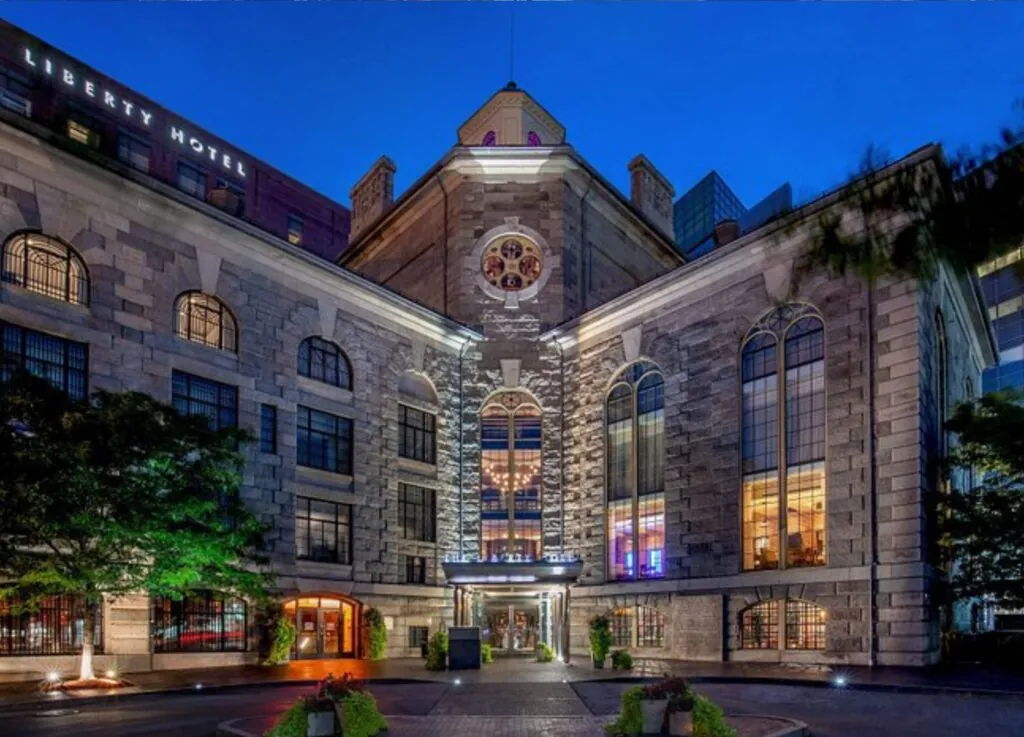 Historic stone hotel with arched windows and central clock, illuminated at night in Beacon Hill; photo captures the Liberty Hotel sign.