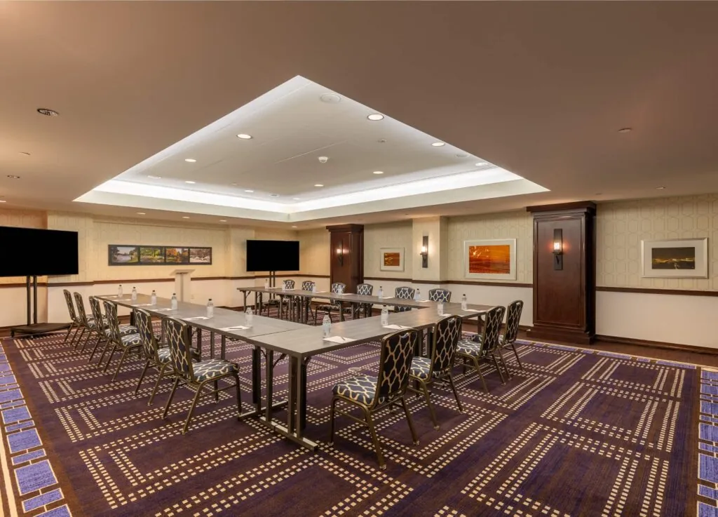 Luxury conference room in a hotel near Beacon Hill, with U-shaped table, TVs, notepads, and chic art under bright lights.