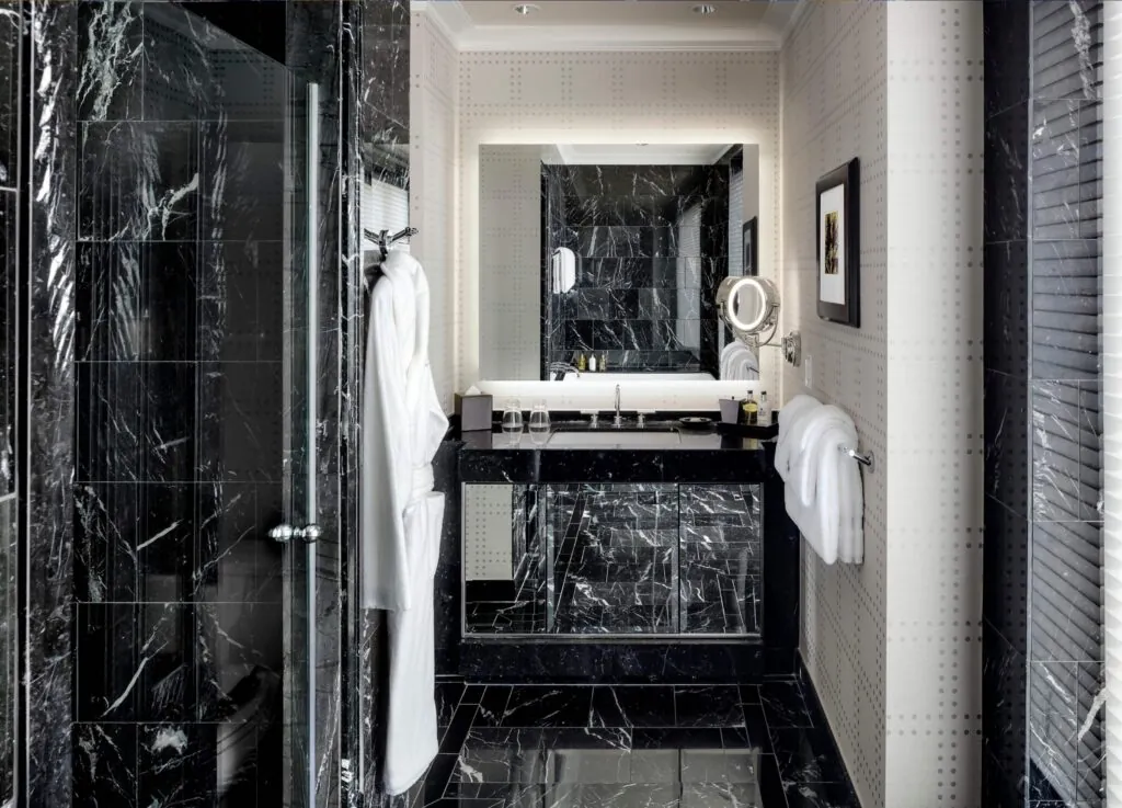 Luxury modern bathroom with black marble, glass shower, white hotel bathrobes, large mirror, and gallery-style neatly folded towels.