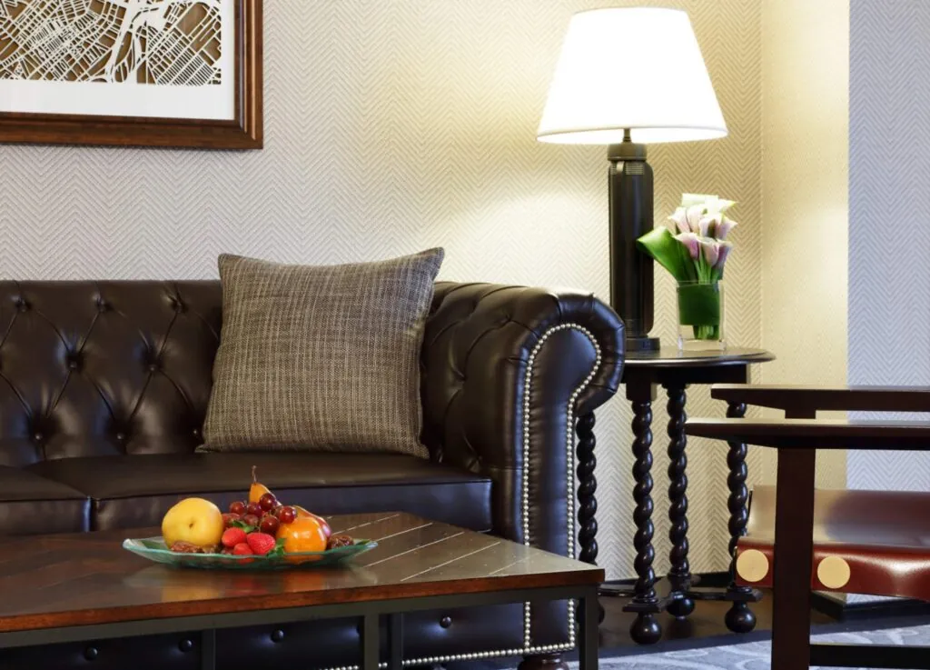 A luxury dark leather sofa with a gray pillow, fruit plate, and lamp create a cozy setting; photo taken in an elegant Beacon Hill living room.