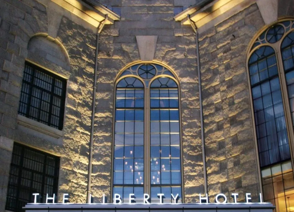 The Liberty Hotel sign glows under tall arched windows on a luxury stone building in Beacon Hill at night.
