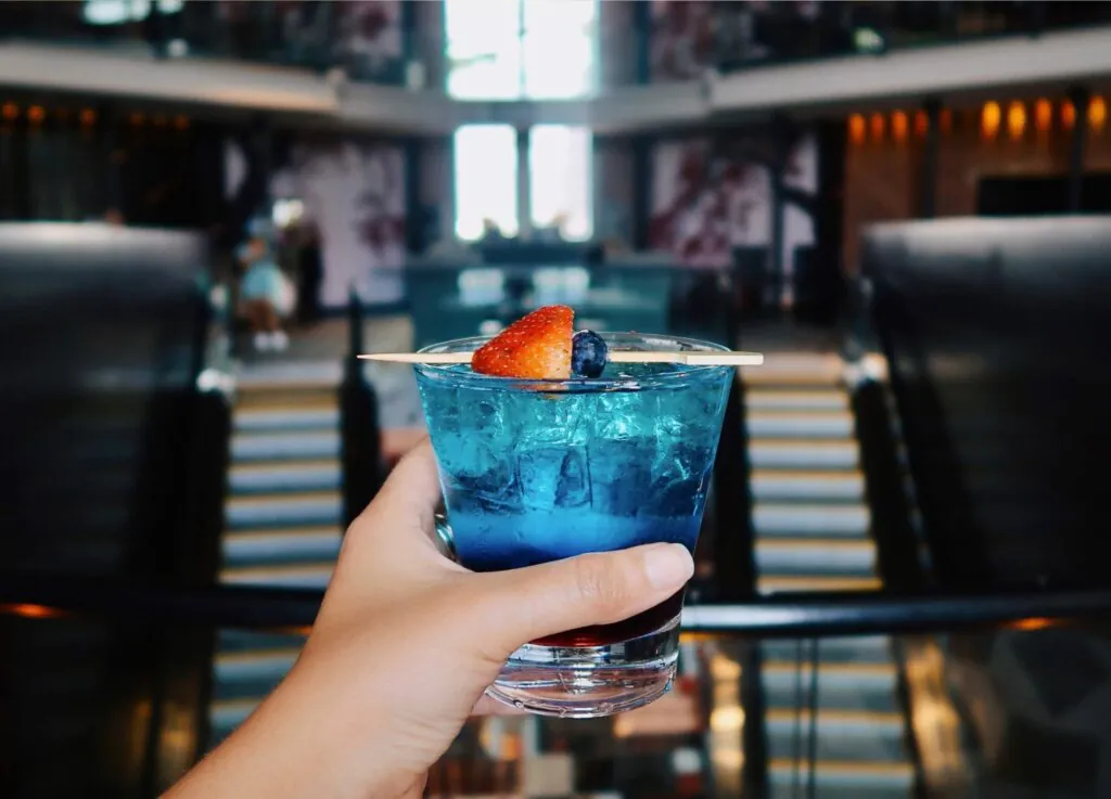 A hand holds a blue cocktail garnished with berries, set against a luxury staircase in a chic Beacon Hill interior.