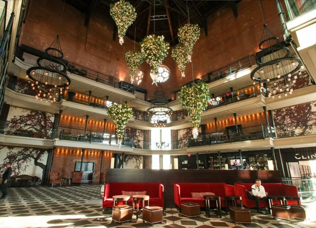 Spacious hotel lobby with high ceilings, floral chandeliers, red seating, patterned floor—like a photo gallery near Beacon Hill with a single guest relaxing.