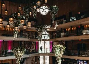 A couple stands on a balcony at a Beacon Hill hotel, surrounded by chandeliers, brick walls, and stunning floral arrangements—perfect for a photo.