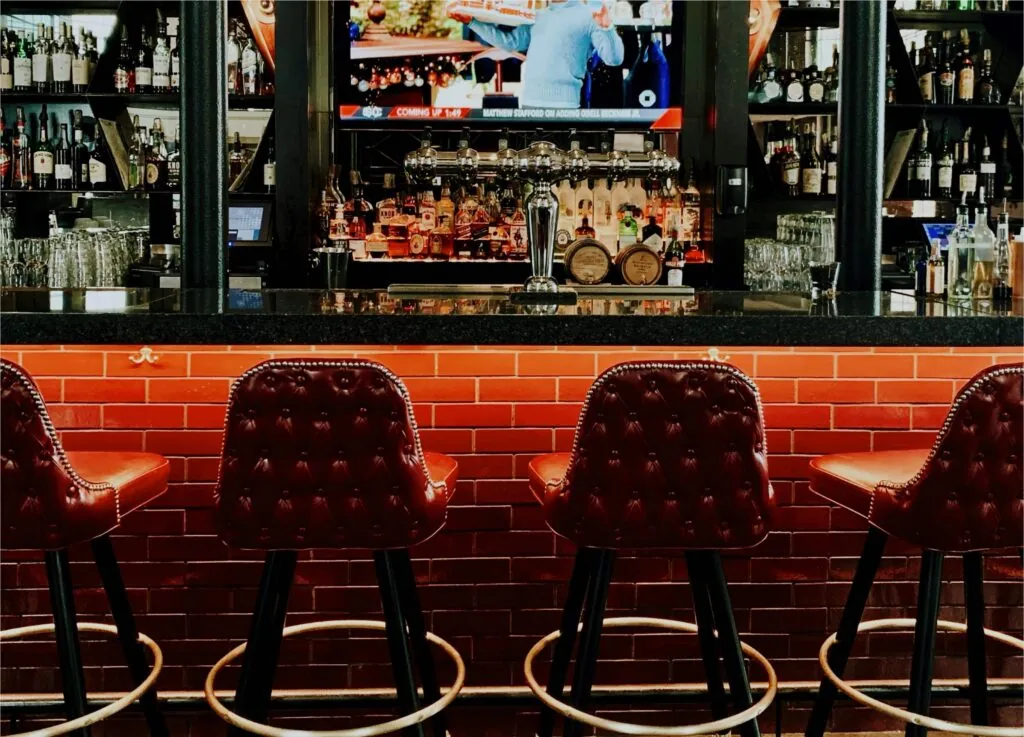 Luxury photo: Four red leather barstools line a bar with red tile front, shelves of liquor bottles, and a TV—perfect for Beacon Hill style.