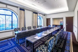 Conference room meeting space with U-shaped table, blue chairs, notepads, glasses, and large arched windows overlooking Boston Common.