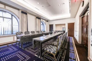 A bright, modern conference room near Beacon Hill with arched windows, patterned carpet, and chairs arranged around tables set for a meeting.