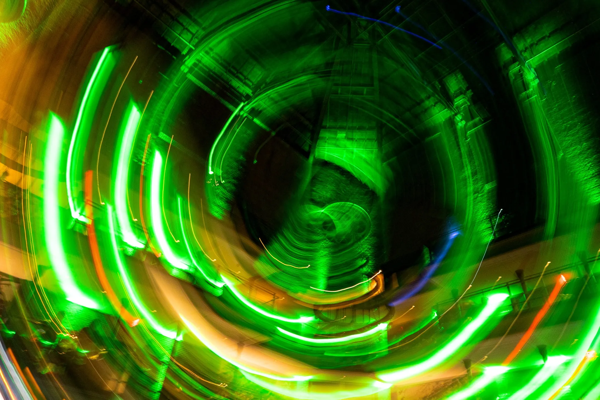 Green and yellow light trails swirl in abstract circular patterns against a dark background, creating a vibrant, dynamic motion effect.